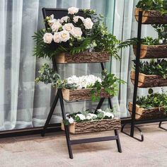 three tiered plant stand with white flowers and greenery in them on the floor