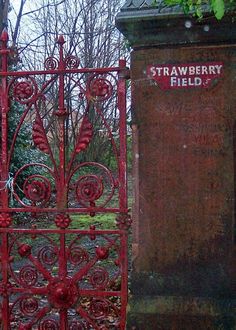 an old red iron gate with the word strawberry field written on it next to a grave