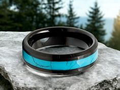 a black and blue wedding ring sitting on top of a rock with trees in the background