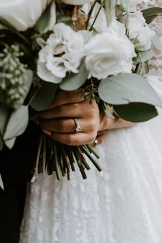 a person holding a bouquet of flowers and greenery in their hands, with the bride's wedding ring on her finger