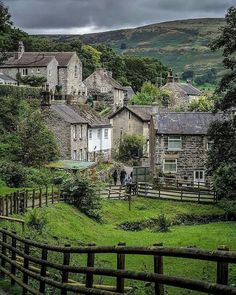 the village is surrounded by lush green hills and trees, with people walking in the distance