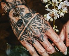 two hands with tattoos and flowers on their palms, one is holding the other's hand