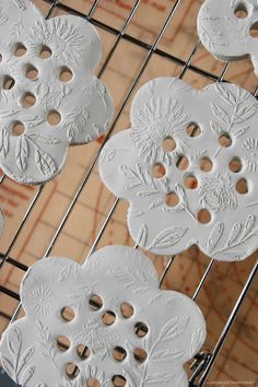 some white buttons are sitting on a wire rack with holes in the middle and flowers carved into them