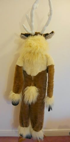 a stuffed animal with horns and fur on it's back standing in front of a wall