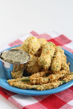 some fried food on a blue plate with a dipping sauce in the middle and a red checkered tablecloth