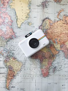 a polaroid camera sitting on top of a map with the world in the background