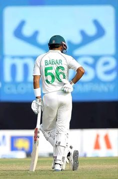 a man standing on top of a green field holding a cricket racquet in his hand