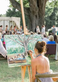 a woman sitting in front of an easel painting a tree with people on it