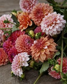 a bunch of pink and orange flowers sitting on top of a wooden table next to green leaves