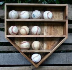 a wooden shelf with baseballs in it on top of some wood planks next to a tree