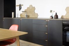 a kitchen with black cabinets and orange chairs next to a table in front of an oven