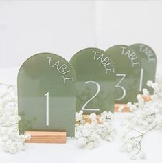 the table numbers are green and have white flowers in front of them on wooden stands