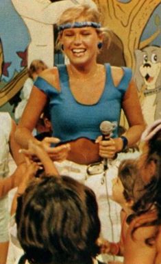 a woman in blue shirt holding a microphone surrounded by children