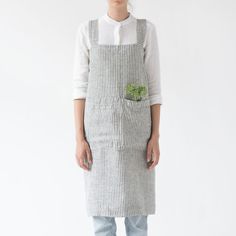 a woman standing in front of a white wall wearing an apron with a green leaf on it