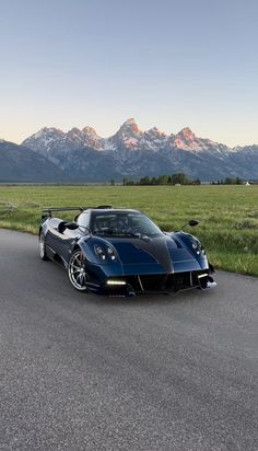 a black and blue sports car driving down a road with mountains in the back ground