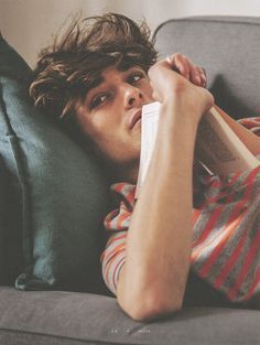 a young man laying on top of a couch holding a book