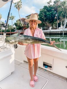 a woman in pink shirt holding up a fish while standing on boat with palm trees