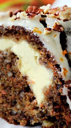 a piece of carrot cake with white frosting and nuts on top, sitting on a plate