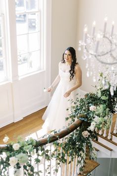 a woman in a wedding dress is standing on the stairs with flowers and greenery