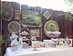 a table topped with plates and cakes next to a wooden fence covered in mirrors on it's side