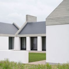 two white houses sitting next to each other on top of a lush green field with tall grass