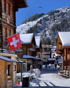 a town with snow covered mountains in the background and people walking down the street on either side