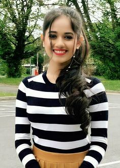 a woman standing in a parking lot wearing a striped shirt and tan pleated skirt