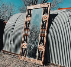 an old mirror sitting on the side of a metal building in front of a tree