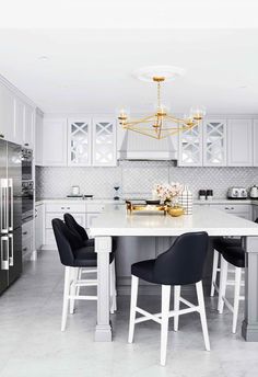 a white kitchen with black chairs and a chandelier hanging from the center island