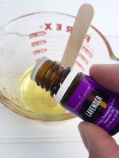 a hand is holding an essential oil bottle in front of a bowl with spoons