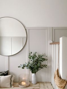 a table with a mirror, vase and candle on it in front of a white wall