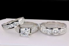 two wedding rings with princess cut diamonds on them sitting on a white box, ready to be purchased