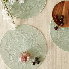 two round placemats with crocheted designs on them next to a small bowl of grapes