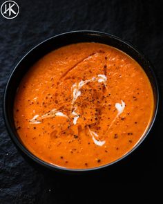 a black bowl filled with red soup on top of a dark tablecloth next to a spoon