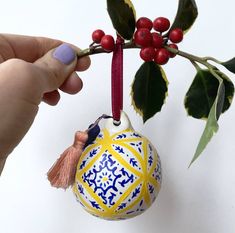 a hand holding a christmas ornament with berries and leaves on the tree branch