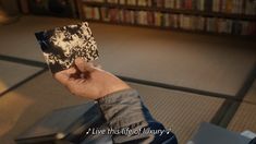 a person holding up a piece of paper in front of a book shelf filled with books