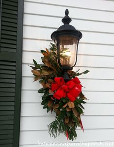 a christmas wreath hanging on the side of a house next to a street light with red bows