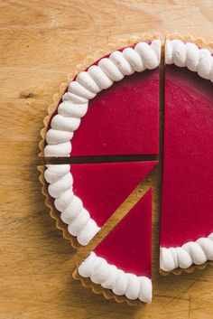 a red and white pie on a wooden table with one slice missing from the pie