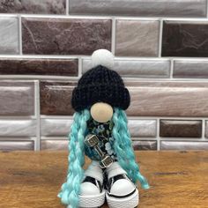 a doll with blue hair and black hat sitting on top of a wooden table in front of a brick wall