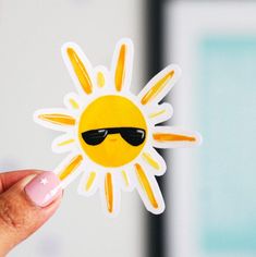 a person holding up a sticker with the shape of a sun wearing sunglasses