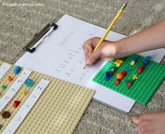 a child's hand is writing on paper next to legos