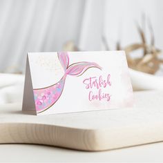 a card with a pink mermaid tail on it sitting on top of a wooden board