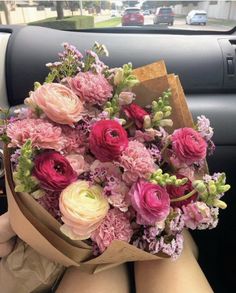 a woman holding a bouquet of pink and white flowers in her lap while sitting in the back seat of a car