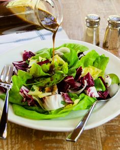 lettuce salad with dressing being poured onto it and sitting on a white plate