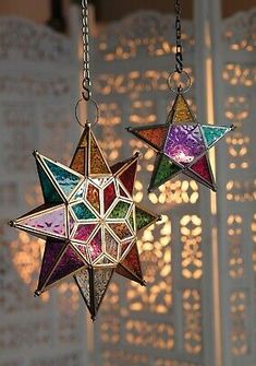 two multicolored stars hanging from chains in front of a white wall with laser cut screens