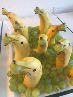 some bananas and grapes are arranged in the shape of birds on a glass plate with green grapes