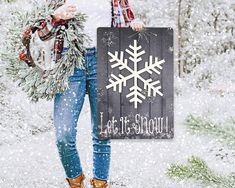 a woman standing in the snow holding a sign that says let it snow and wreath