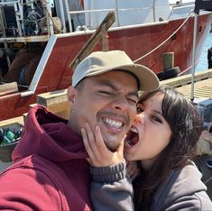 a man and woman standing next to each other in front of a boat