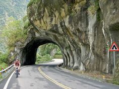 a man riding his bike into a tunnel on the side of a road with mountains in the background