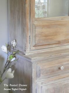 a vase with flowers in it sitting next to a wooden cabinet and mirror on the wall